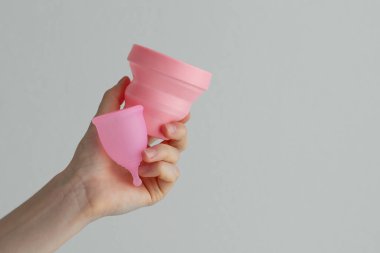 Pembe bir adet bardağının üst görüntüsü ve beyaz bir arka planda dezenfeksiyon için bir kap. Adet sırasında kadın hijyeni için yeniden kullanılabilir ürünler kavramı