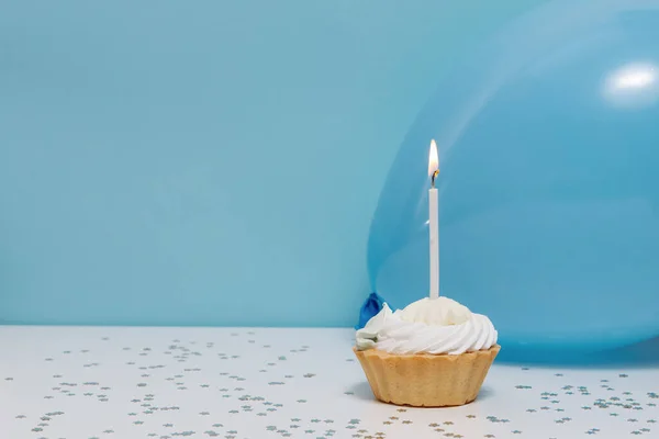 Mavi arka planda bir mum, balon ve şenlikli bir dekoru olan doğum günü pastası. Tasarımınız için arkaplan