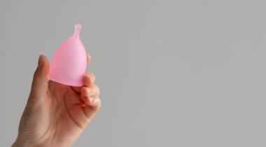 Beyaz izole edilmiş arka planda bir kadının elinde regl bardağı. Regl sırasında ve kritik günlerde pedlere ve tamponlara uygulanabilir bir alternatif. Tasarımınız veya modeliniz için yer