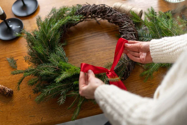 一个穿着针织毛衣的女人用松枝做了一个可爱的圣诞花环 并用红丝带绑在上面 圣诞节的替代树 假日概念 — 图库照片