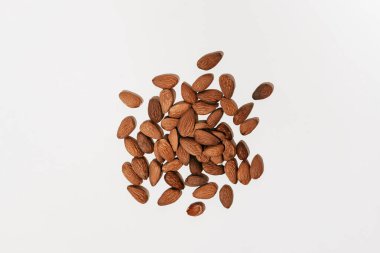 Scattered brown almonds illuminated by hard daylight on a white isolated background. Ingredient for cosmetics and image for design