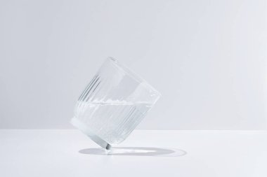 Tilted clear glass of sparkling water on white isolated background in daylight. Elegant image for your design