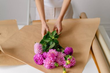 Genç bir çiçekçi kadın hediye olarak kahverengi kraft kağıdında bir buket pembe yıldız çiçeği topluyor. Tasarımınız için yatay görüntü. Baharın gelişi konsepti