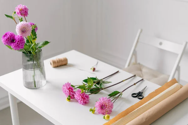 Florist\'s tools and delicate pink dahlias lie on a white table in preparation for creating a bouquet indoors. Image for your design