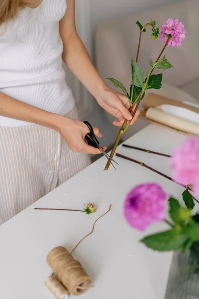 A young woman florist cuts the end of a pink flower with scissors to add it to a bouquet. Vertical image for your design. Small business concept