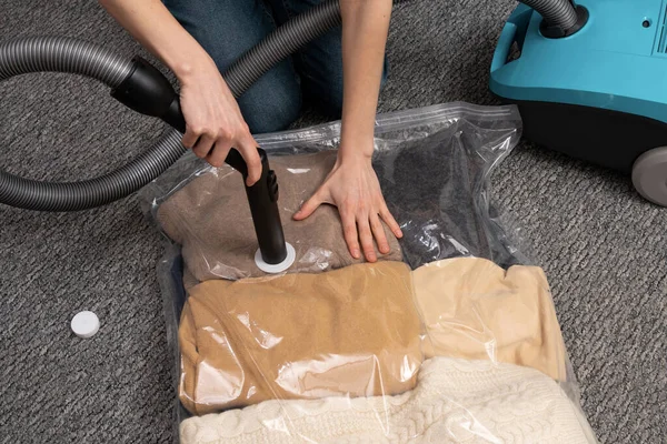 A young woman uses a vacuum cleaner to extract air from a transparent vacuum bag with warm things. Hermetic bag for saving space and storing clothes under vacuum