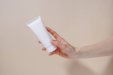 Bej izole arka planda beyaz, boş bir krem tüpünü tutan bir kadın el. Güzellik ve estetik kavramı. Kozmetik ürün markalaşma modeli. Tasarımın için resim