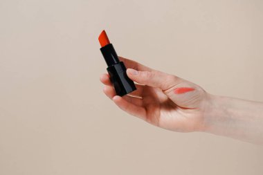 Bej izole arkaplanda kumaş parçalı kırmızı ruj tutan bir kadın. Dekoratif kozmetik, güzellik ve estetik kavramı