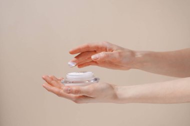 Kadın eli, cam kavanozdan beyaz nemlendirici krem sürüyor. Bej izole arka planda parmak üstüne. Güzellik, cilt bakımı ve estetik konsepti