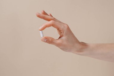 Bej kaplama arka planda parmakları olan beyaz hapları tutan bir kadın. Sağlık hizmetleri kavramı, beslenme takviyeleri, depresyon ve hastalıkların tedavisi