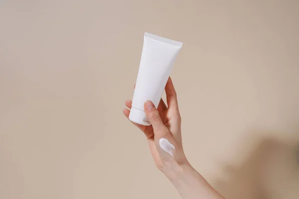 stock image Female hand with smear holding blank mockup tube of cream on beige isolated background. Daily skincare and body care routine. Image for your design