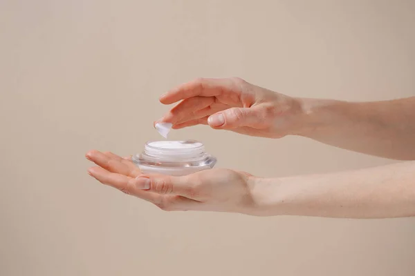 stock image Female hand applying white moisturizing cream from glass jar on finger on beige isolated background. Concept of beauty, cosmetic product, skin treatment and protection