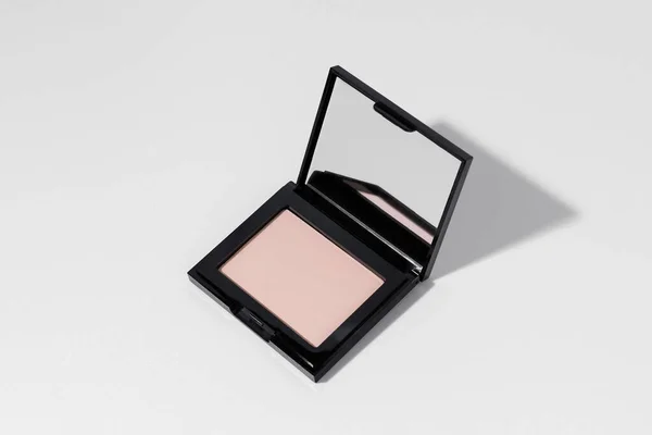 Stock image Pink or peach face powder with mirror with shadow from direct light on white isolated background. Concept of decorative cosmetics for face makeup, cosmetic product. Image for your design.