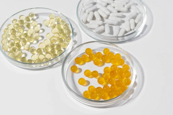 stock image Laboratory petri dishes with yellow, orange and white pills on gray isolated background. Concept of dietary supplements, vitamins to improve health