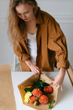 Genç çekici bayan çiçekçi, kahverengi kraft kağıdıyla dikey imgeye yıldız çiçeği sarıyordu. Küçük işletme kavramı