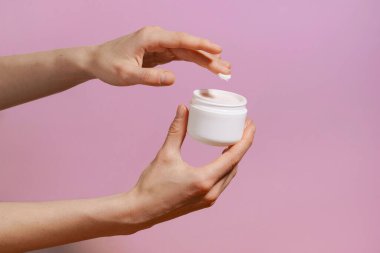 Dişi narin el, mor izole arka planda tuttuğu beyaz bir maket kavanozundan krem alır. Güzellik ve estetik kavramı, doğal kozmetik. Tasarımın için resim