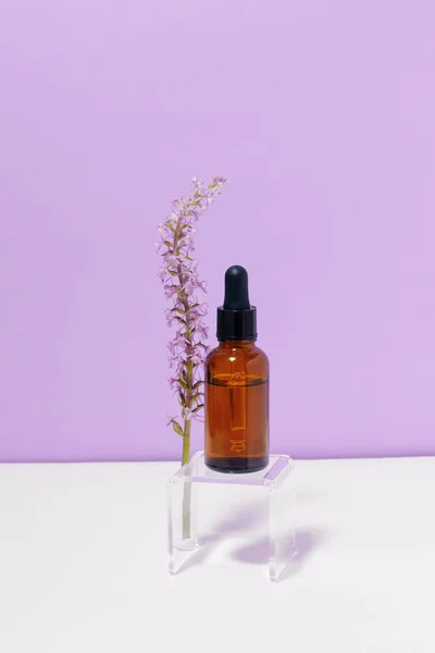 stock image Vertical image of a glass transparent jar of facial serum with a flower on a purple background. Concept of face cosmetics, natural ingredients and beauty