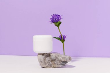 Beyaz süsleme kavanozu. Doğal krema ya da tereyağı. Mor arka planda çiçek olan bir taşın üzerindeki yüz derisi için. güzellik, kaplıca ve vücut bakımı konsepti