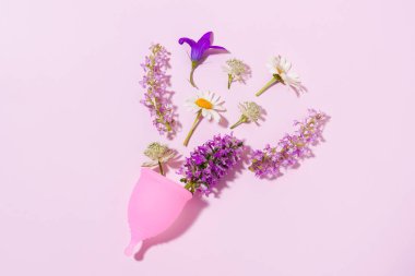 Pembe aybaşı fincanı, pembe izole edilmiş arka planda çiçekler. Adet döngüsü için hijyenik kadın ürünleri kavramı ve pedlere ekolojik bir alternatif.
