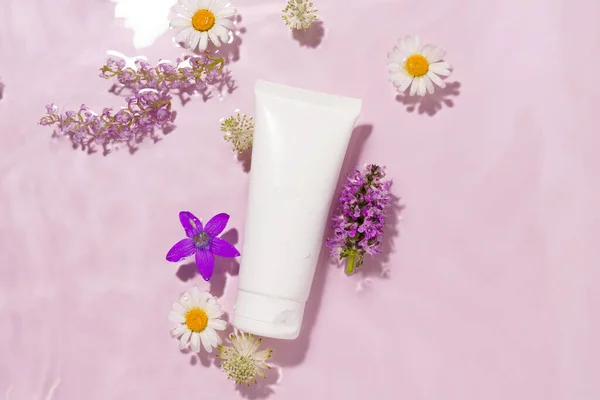 White blank mockup of a tube of cream in the texture of water on a pink background. The concept of cosmetics for beauty, moisturizing and restoring the skin. Presentation of a new product