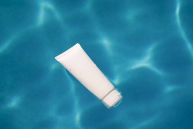 Bir tüp nemlendiricinin beyaz modeli ya da güneş ışığıyla aydınlatılmış mavi havuz suyunda yüzen güneş kremi. Yüzün ve vücudun cildinin güzelliği, korunması ve nemlendirilmesi..