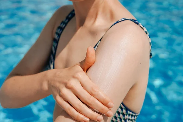 一位年轻女子在蓝色池水的背景下把防晒霜涂在皮肤上 美容美发 度假等概念 — 图库照片