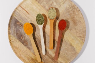 Ahşap kaşıklarda tütsülenmiş zerdeçal, kırmızı biber ve fesleğen ve beyaz izole arka planda bir tabak yakın plan. Tasarımınız için görüntü. Aromatik yemek pişirme