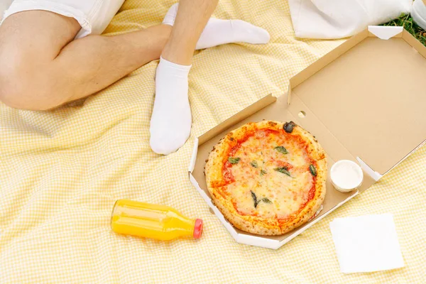 Close-up of man on picnic with pizza in box and orange or multivitamin juice mockup. Concept of food delivery, outdoor recreation, fast snack