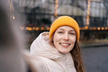 Genç ve çekici bir kadın telefonda çelenk ve gülücüklerin arka planına karşı selfie çekiyor. Yeni yıl ve mucizeler konsepti