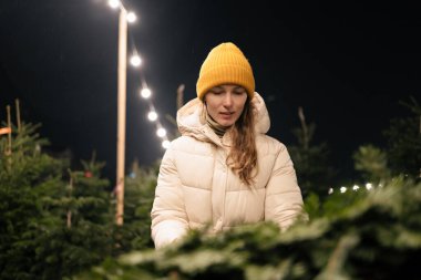 Genç bir kadın akşamları markette Noel ağacı dallarını seçer. Yeni yıl ve kış tatili kavramı