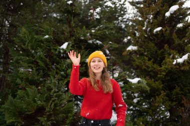 Dışarıda Noel ağaçlarının arka planında kartopu oynarken örgü örülü süveter giyen genç bir kadın. Kış aktiviteleri ve tatil konsepti