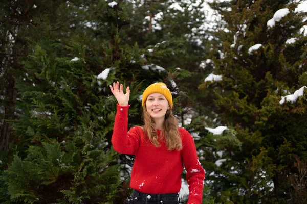 Dışarıda Noel ağaçlarının arka planında kartopu oynarken örgü örülü süveter giyen genç bir kadın. Kış aktiviteleri ve tatil konsepti