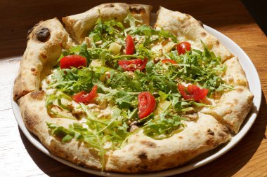 Domatesli İtalyan pizzası ve öğlen güneşiyle aydınlatılmış roka. Lokantada atıştırmalık ve lezzetli yemekler konsepti