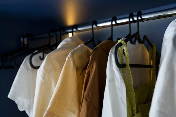 Close-up of dress and shirt hanging on black hangers in backlit closet. Clothes storage concept. Image for your design