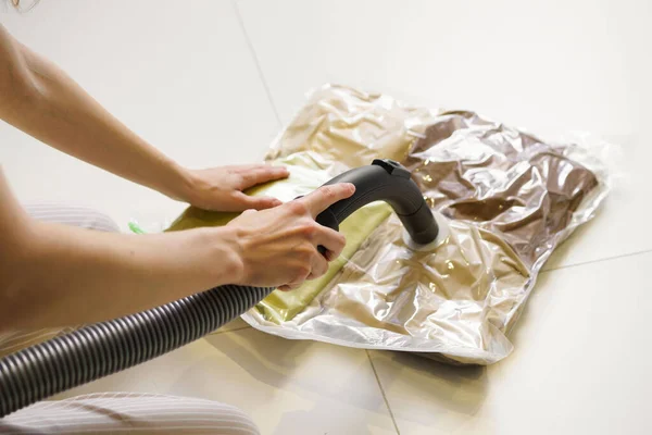A woman\'s hands remove air with a vacuum cleaner from a vacuum bag with clothes on the floor. The concept of compact storage and transportation of clothes.