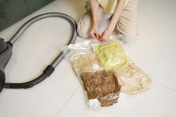 A young woman opens a transparent sealed bag with clothes to get things after seasonal storage. The concept of storing and transporting clothes under vacuum