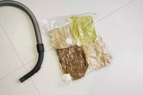 Top view of a vacuum bag with clothes and a vacuum cleaner hose on the floor. The concept of storing things under sealant and saving space in the closet
