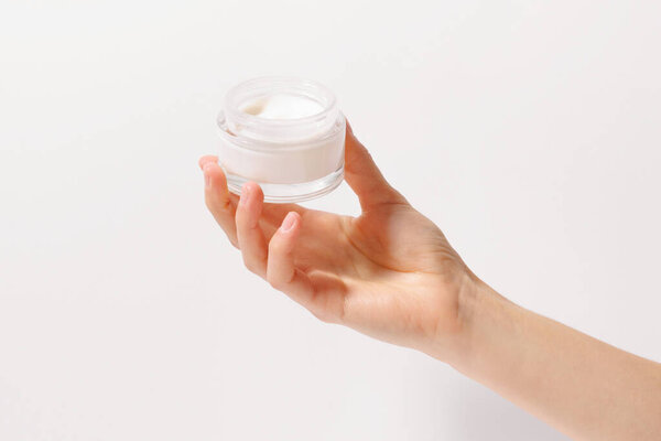 Female hand holding glass jar of face cream on white isolated background. The concept of moisturizing and nourishing the skin, beauty products, skin care