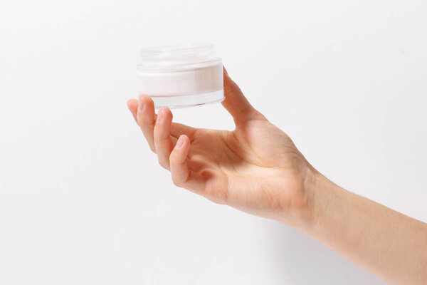 Close-up of a female hand holding a transparent mockup jar of face cream on a white isolated background. Concept of beauty products to moisturize and nourish the skin. Image for your design