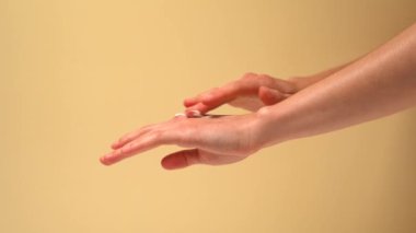 Dişi eller, kremi parmaklarıyla sürerler ve bej izole arka planda cildine sürerler. Güzellik ve estetik kavramı, deriyi nemlendirip besler.