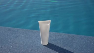 Gündüz güneşiyle aydınlanan bir krem tüpünün beyaz modeli bir yüzme havuzundaki mavi suyun arka planında. Yüz ve vücut derisi için nemlendirici ve güneş kremi kavramı, güzellik