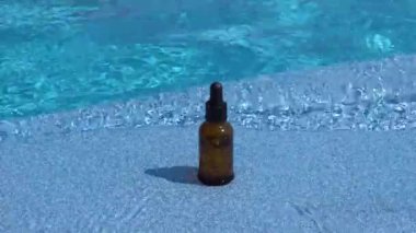 Yüzme havuzundaki dalgalı mavi suyun arka planında yüz derisi için damlatan kahverengi cam serum kavanozu. Yüz derisi için nemlendirici ve besleyici kozmetik konsepti.