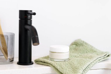 Havlunun üzerinde beyaz bir krema kavanozu ve banyoda bir lavabo. Yüz ve vücut bakımı kavramı, günlük rutin ve güzellik ürünleri