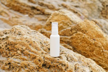 Beyaz boş serum kavanozu ya da deniz kenarındaki sarı kireç taşının üzerindeki yüz kremi. Cilt, güzellik ve bakım kozmetik ürünlerini nemlendirmek ve korumak için kullanılan doğal ürünler kavramı