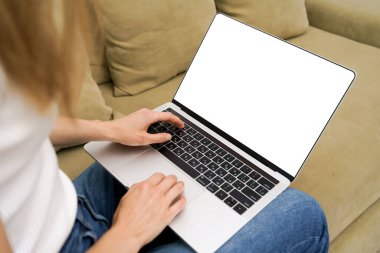 Kanepede otururken dizüstü bilgisayarında beyaz bir ekran ile yazı yazan genç bir kadının yatay görüntüsü. Uzaktan kumanda konsepti. Tasarımın için resim