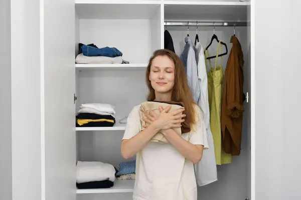A young attractive woman hugs her favorite clothes standing against a closet with things. The concept of changing seasonal wardrobe, charitable donations of clothes