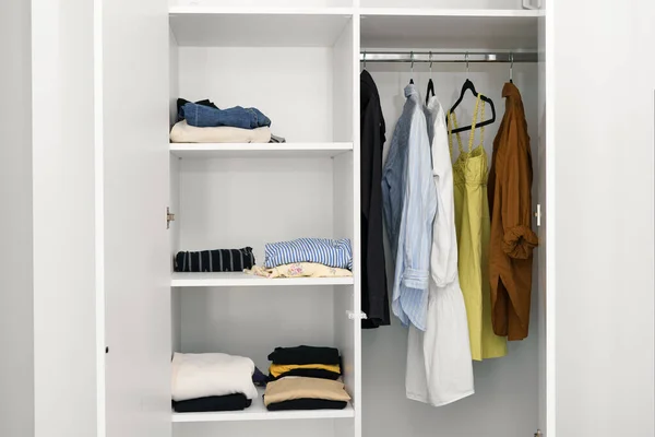 Women\'s wardrobe in the white closet - neatly folded t-shirts and sweaters, dresses on hangers. the concept of compact storage of clothes and organization of space in the room