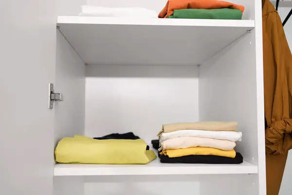 Compactly folded stacks of T-shirts and shirts hanging on hangers in a white closet. The concept of seasonal wardrobe replacement, efficient storage and use of space