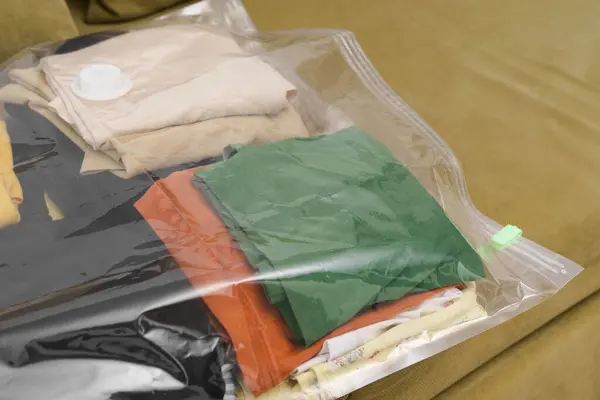 Close-up of a transparent vacuum bag filled with clothes on a green sofa. The concept of compact storage of things and saving space in the closet. Organization of space at home in hermetic bags