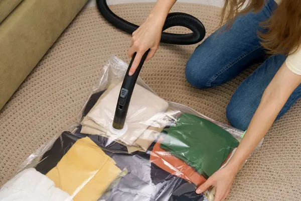 A young woman uses a vacuum cleaner to extract air from a transparent vacuum bag with warm things. Hermetic bag for saving space and storing clothes under vacuum